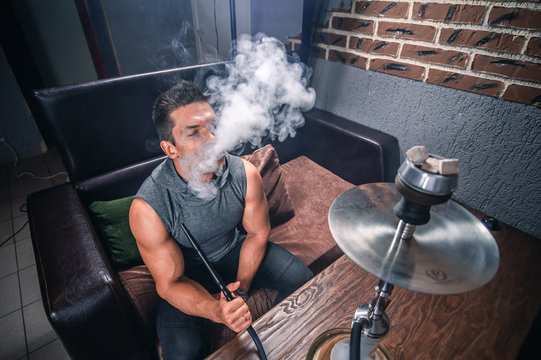 Young handsome man blowing clouds of smoke in the shisha hose.