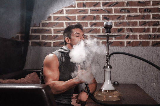Man smokes a fragrant oriental hookah in nightclub.