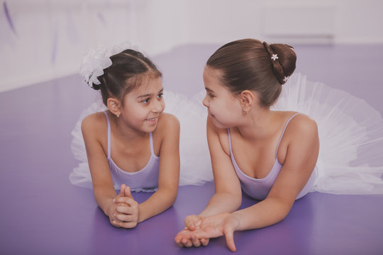 Happy little girls relaxing after ballet class, talking, lying on the floor. Adorbale little ballerinas resting after exercising at ballet school. Young frineds enjoying their break at ballet studio