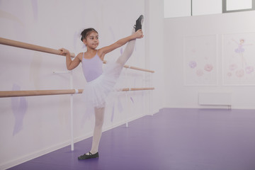 Full length shot of a cute young ballerina stretching at ballet school. Lovely little girl in tutu skirt and leotard exercising  at dancing studio, copy space
