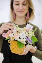 A woman florist in a black apron holds a floral composition in her hands. Young female flower seller smiling looking at bouquet.