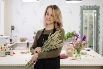 A woman florist in a black apron holds a floral composition in her hands. Young female flower...