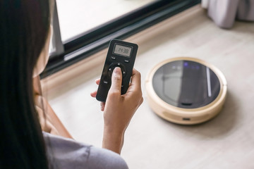 Close-up of a woman Holding remote control controls a robotic vacuum cleaner on the floor