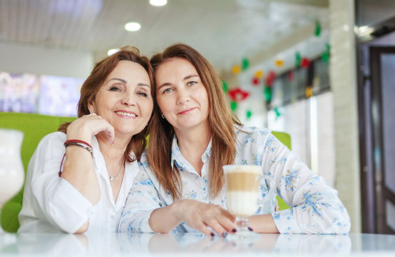 Two attractive happy middle-aged women girlfriends spend time in a cafe, chat and friendship