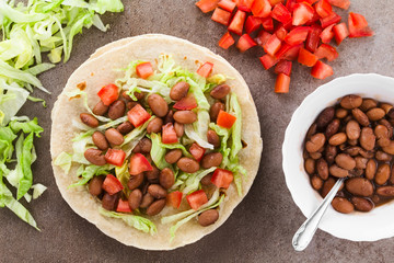 Fresh homemade vegan tacos made of flour tortilla with lettuce, cooked beans and tomatoes, photographed overhead