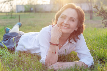 Beautiful happy smiling elderly mature senior 60 years woman lying on the grass, summer vacation