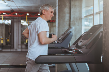 Senior sportsman running on a treadmill at the gym, copy space. Healthy elderly man enjoying working out at sport studio, jogging on a running machine. Cardio, endurance, health concept