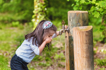 little girl drinks water from a wooden tap