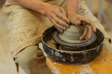 Strong man with dirty hands sitting on wooden pottery wheel