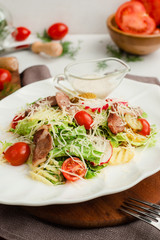 Salad with roasted meat, radish, lettuce, cherry tomatoes, cheese, and pickled cucumbers. Cafe menu on a wooden background in warm colors.