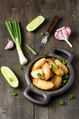Young fried potatoes, green onions, fresh cucumbers and garlic on a dark wooden background. Selective focus.