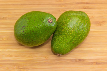 Two whole green avocado fruits on a wooden cutting board