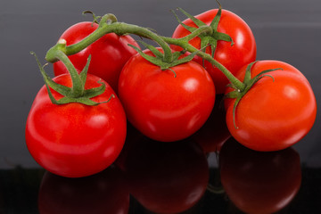 Red tomatoes on branch on a dark reflective surface