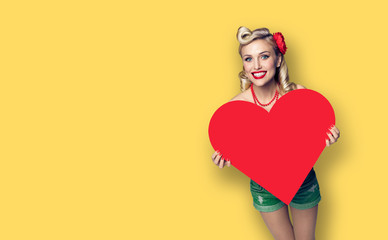 Photo of happy smiling woman holding red paper heart shape, over yellow color background. Copy space.