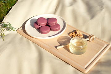 Many colored french macaroons or macaroon on a wooden tray a jar of honey and a round wooden spoon for honey.