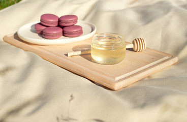 Obraz na płótnie Canvas Many colored french macaroons or macaroon on a wooden tray a jar of honey and a round wooden spoon for honey.