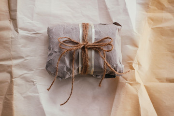 Soft parcel wrapped into old craft paper and tie. Crumpled background texture. Gift shop. Materials for transportation and shipping. 