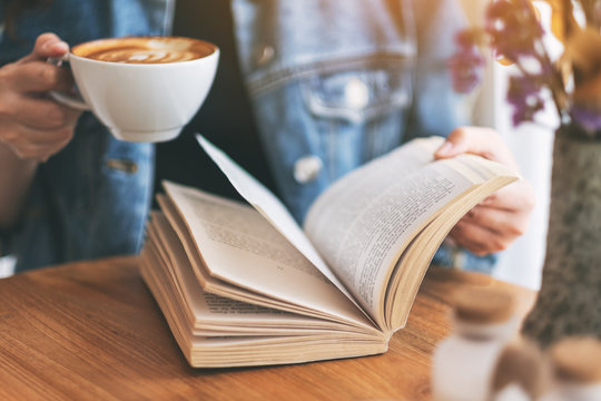 Closeup image of a woman holding and reading a vintage novel book while drinking coffee