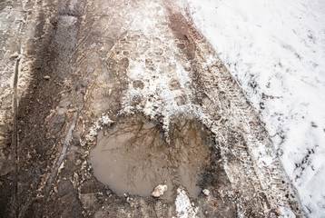Melting snow on the road. Dirty mud with puddle. Winter weather concept.