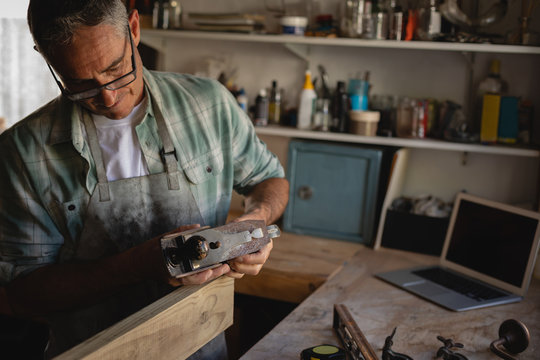 Mature carpenter using smooth plane on wooden plank in workshop