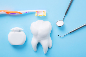 Dental health and teethcare concept. Professional steel dental instrument with a mirror near white tooth model, toothbrush and dental floss on light blue background.