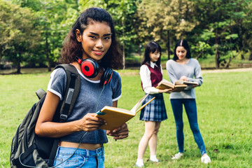 Smiling woman international students or teenagers standing and holding book smiling at camera with group of students in park at university.Education and friendship Concept