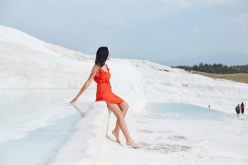 Girl in red dress on white travertines, water