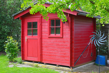 Rot gestrichenes Gartenhaus unter einem Baum in einer häuslichen Gartenanlage, 