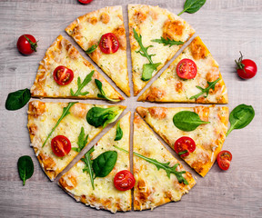 tasty sliced pizza with tomatoes and herbs over wooden table background