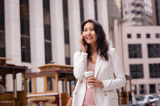 Beautiful woman talking on mobile phone while having coffee on street