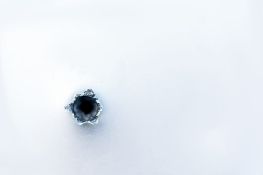 Bullet hole on the metal fragment from the white surface