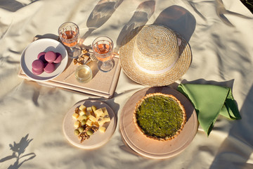 Fototapeta na wymiar Picnic basket with fruit and macaroon bakery transparent glasses of drink on a beige fabric in the garden.