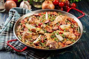Traditional paella with chicken legs, sausage chorizo and vegetables served in paellera
