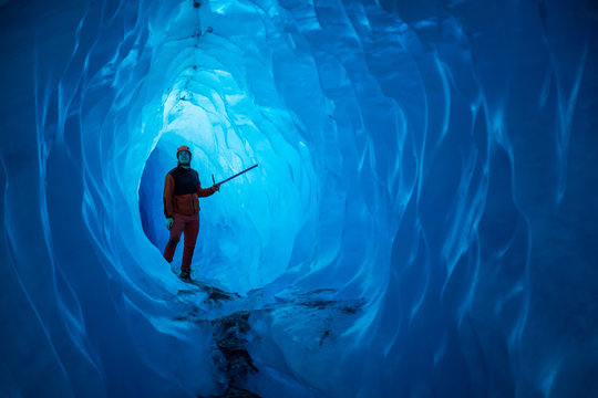 Man inside a melting glacier ice cave. Cut by water from the melting glacier, the cave runs deep into the ice of the Matanuska Glacier in Alaska.