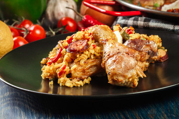 Traditional paella with chicken legs, sausage chorizo and vegetables served on black plate
