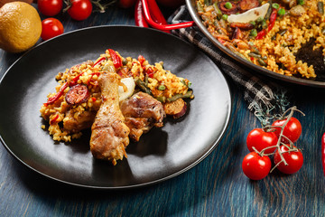 Traditional paella with chicken legs, sausage chorizo and vegetables served on black plate