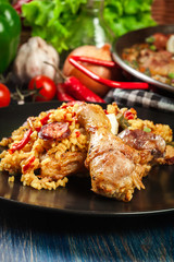 Traditional paella with chicken legs, sausage chorizo and vegetables served on black plate
