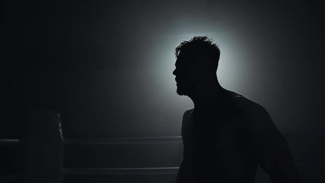 Angry man with boxing gloves emotionally standing on the boxing ring. Slow, motion, silhouette. Boxing concept.