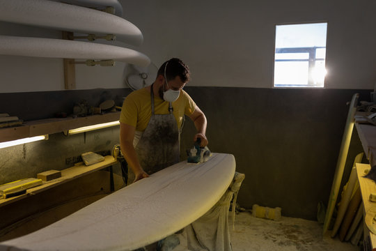 Man shaping surfboard in a workshop