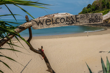 A view of a  beach with a rustic welcome sign on the island of Koh Lanta, Thailand, the beach is totally empty and idyllic with the sparkling Andaman Sea, nobody in the image