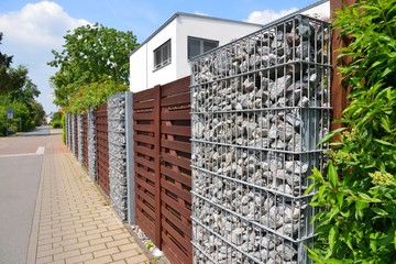 Moderner Sichtschutzzaun aus mit Naturstein gefüllten Gabionen, Holzbretterverschalung und...