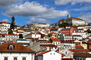 Panorama of Coimbra town, former medieval capital of Portugal. View of old colorful roofs and houses and university campus with clock tower over blue sky with clouds. European travel concept.