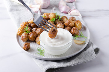 Process of dunking fried hot potato in delicious sauce.Plate full of fried new potatoes,dill,bowl with sauce, napkin on the white table