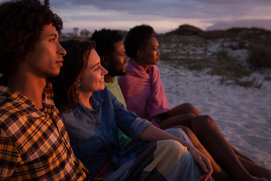 Friends group sitting on beach while they are looking away ocean