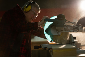 Carpenter with headset cutting a piece of wood with a mechanic saw at workshop