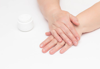 Obraz na płótnie Canvas The hands of an elderly woman on a white background and a complex cream with vitamin against wrinkles and tightness on the skin of the hands, restoring the epidermis, strengthening the protective