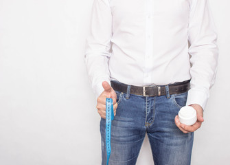 A man on a white background holds a centimeter tape and cream on the background of the penis, the...