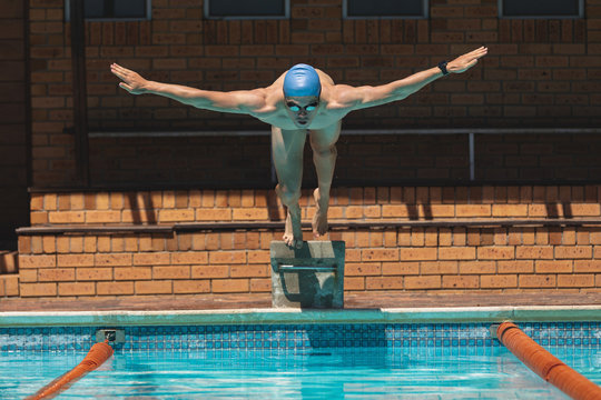 Young Caucasian male swimmer with arms stretched out jumping into swimming pool