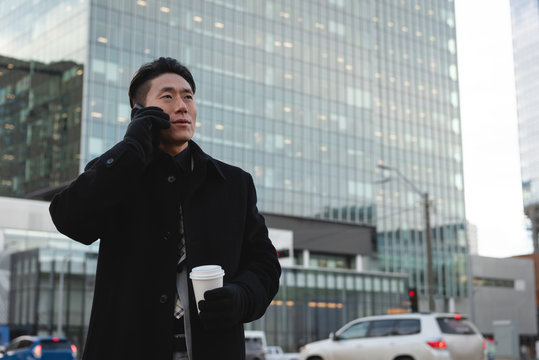Young Asian male businessman talking on mobile phone while holding a coffee in hand