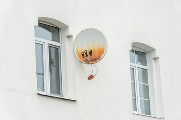 Rusty satellite dish on the white wall of the house with windows close-up
